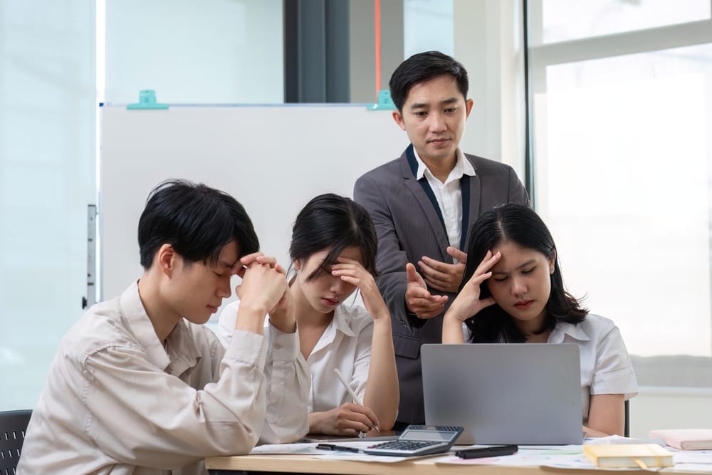 Asian office team under pressure reviewing figures on a laptop and calculator while a manager explains a severance pay calculation